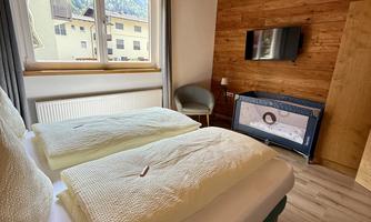 A cozy bedroom with two single beds and wooden ceilings. A television and a chair complement the space.