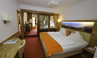 A cozy hotel room with a double bed and orange accents. In the background, there is a desk and a comfortable chair.