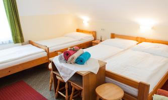 A cozy room with three beds, a table, and chairs. There are colorful towels and a pleasant atmosphere created by the daylight.
