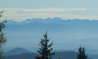 A picturesque mountain landscape with snow-covered peaks. The sky is clear and there is a gentle mist over the valleys.