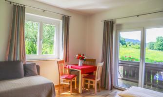 A bright room with a table and chairs as well as a cozy sofa. Large windows offer a view of the green landscape.