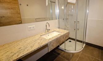A modern bathroom with an elegant shower cabin and a granite sink. The walls are light, and the floor has dark tiles.