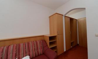 A simple room with a red sofa and wooden furniture. There is storage in the form of cabinets and shelves.