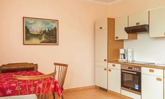 A cozy kitchen with a red table and wooden benches. A landscape painting is hanging on the wall, and the kitchen is modernly furnished.
