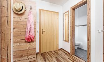 An inviting hallway with wooden walls and a warm floor. A door leads to a bathroom, and a hat and a pink bathrobe hang on the wall.