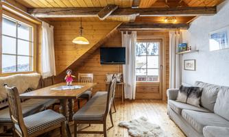 A cozy living space with wood paneling and a dining table. The sun shines through the windows, creating an inviting atmosphere.