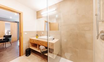 A modern bathroom with a glass shower and a wooden washbasin. The walls are painted in neutral tones.