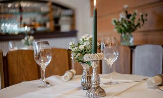 An elegant table in a restaurant with a green candle, a floral arrangement, and wine glasses. The tablecloth is white and the surroundings convey an inviting atmosphere.
