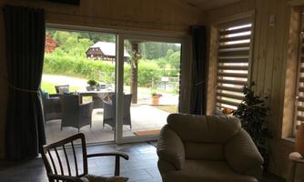 A cozy interior with a comfortable armchair and a view of a terrace. Outside, you can see green meadows and a few garden furniture.