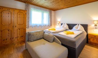A cozy bedroom with a wooden ceiling and two single beds. Next to the bed is a couch and a wooden box.