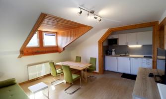 A modern apartment with wooden elements and plenty of light. The space features a dining area, a kitchenette, and cozy furniture.