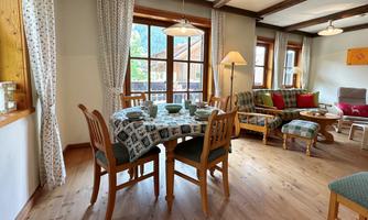 A cozy living space with a dining table and chairs. Large windows provide a view of the outdoors and let in plenty of light.