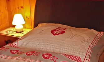 A cozy bed with a decorative blanket and a pillow. Next to the bed is a small lamp that provides warm light.