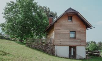 A charming wooden house stands on a meadow. In the background, a large tree can be seen.
