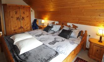 A cozy bedroom with a large wooden bed and decorative pillows. The walls are paneled with wood, and there is soft lighting from the table lamps.