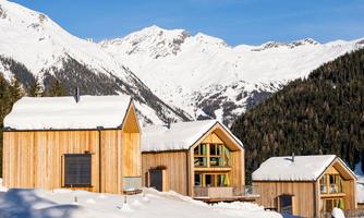 A picturesque mountain landscape with snow-covered cottages. In the background, majestic mountains rise under a clear sky.