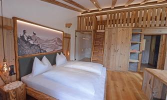A cozy bedroom with two beds and wood paneling. The walls are made of natural wood, and there is a staircase leading to an upper area.