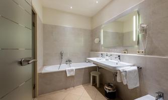 A modern bathroom with a bathtub and two sinks. The walls are in neutral tones and there is a lighted mirror.