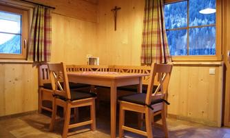 A cozy dining area made of wood with a table and four chairs. The walls are made of wood and there is a window with curtains.