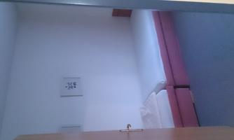 A simple room with two single beds and light-colored walls. There is a door and some pictures on the wall.