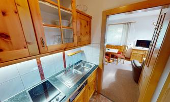 A modern kitchen made of wood with a cooking surface and a sink. The access to a cozy living space is visible.