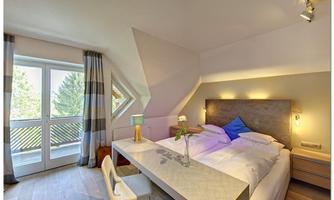 A modern bedroom with a comfortable double bed and desk. Large windows provide plenty of daylight and a view of the outdoors.