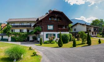 A picturesque country house with a well-kept garden and a clear sky. The surroundings are green and inviting.