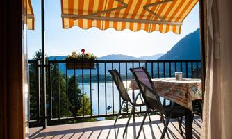 An inviting terrace with a table and chairs. In the background, you can see a beautiful lake and mountains under a clear sky.