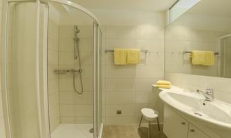 A modern bathroom with a shower and a sink. The walls are painted in light colors, and yellow towels add a splash of color.