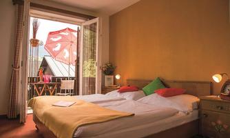 A cozy bedroom with two beds and colorful pillows. The balcony is decorated with a red umbrella and a small table.