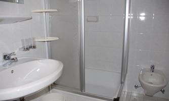 A modern bathroom with a shower, sink, and a bidet. The walls are tiled in light colors, and the design is simple and functional.