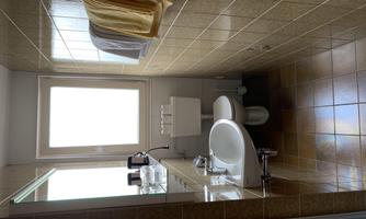 A modern bathroom with a white toilet and a sink. Two towels hang on the wall and there is plenty of daylight coming through the window.