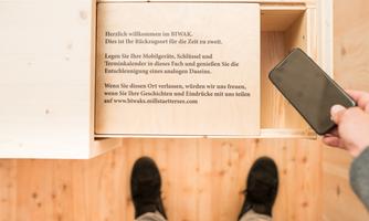 An open wooden drawer with a welcome message. A person is holding a smartphone in their hand.