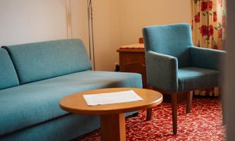 A cozy room with a blue sofa and a chair. The carpet has a blooming pattern and there is a floor lamp as well as a small table.