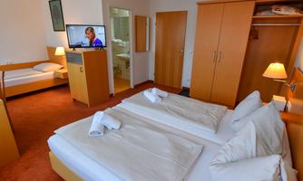 A cozy hotel room with two beds, a television, and a wardrobe. The room is bright and simply furnished, ideal for a pleasant stay.