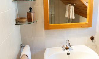 A modern bathroom with a sink and a large mirror. Fresh towels are hanging on the wall and there are shelves with toiletries.