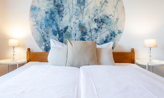 A cozy bedroom with a large bed and beautiful blue wall decor. On both sides of the bed are modern nightstands with lamps.