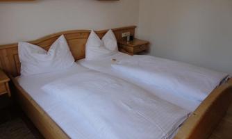 A simple bedroom with two single beds and white bedding. The room features cozy wooden paneling and a desk.