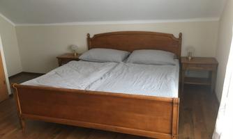 A cozy bedroom with a wooden bed and a textured duvet. Next to the bed are two nightstands with lamps.