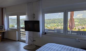 A bright bedroom with a view of a landscape and mountains. Large windows let in plenty of daylight and showcase a beautiful view.