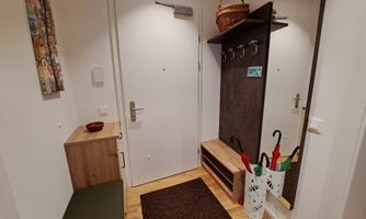 A friendly hallway with a white door and a mirror. Next to a bench, there are coat hooks and a umbrella stand.