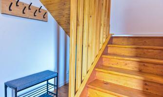A bright hallway with a wooden staircase and a wall coat rack. On the left side, there is a practical bench.