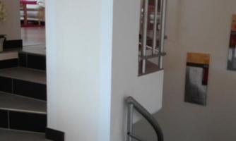 A bright interior with a staircase and modern railings. In the foreground is a wooden surface with decorative objects.