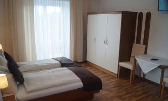 A cozy bedroom with two single beds and a large window. It contains a table, a chair, and a wardrobe.