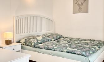 A cozy bedroom with a white bed and colorful bedding. The walls are light, and there is decorative wall art featuring a deer.