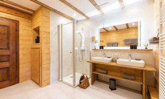 A modern bathroom with wooden paneling and elegant details. It features two sinks and a spacious shower.