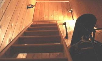 A wooden ladder leads up to a room with wood paneling. A few accessories and a door handle are visible on the wall.