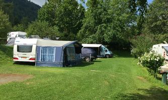 A quiet campsite with several motorhomes and tents. The green meadow and the trees create a relaxed atmosphere.