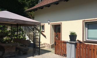 A cozy house with a staircase, surrounded by a garden. Outside, there is a covered seating area and a table.