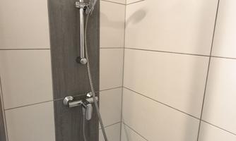 A modern shower cabin with white tiles and a gray wall covering. The shower head and faucet are made of stainless steel.